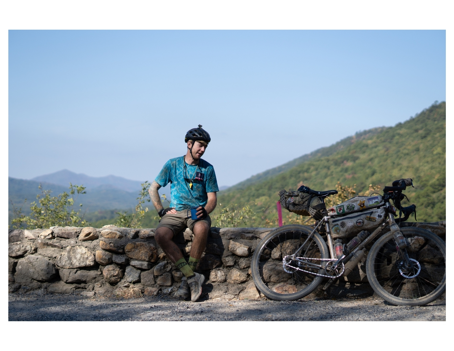 candid portrait of bikepacker resting on a stone wall with his bike at Dix Gap Overlook in arkansas during the Arkansas High Country Race