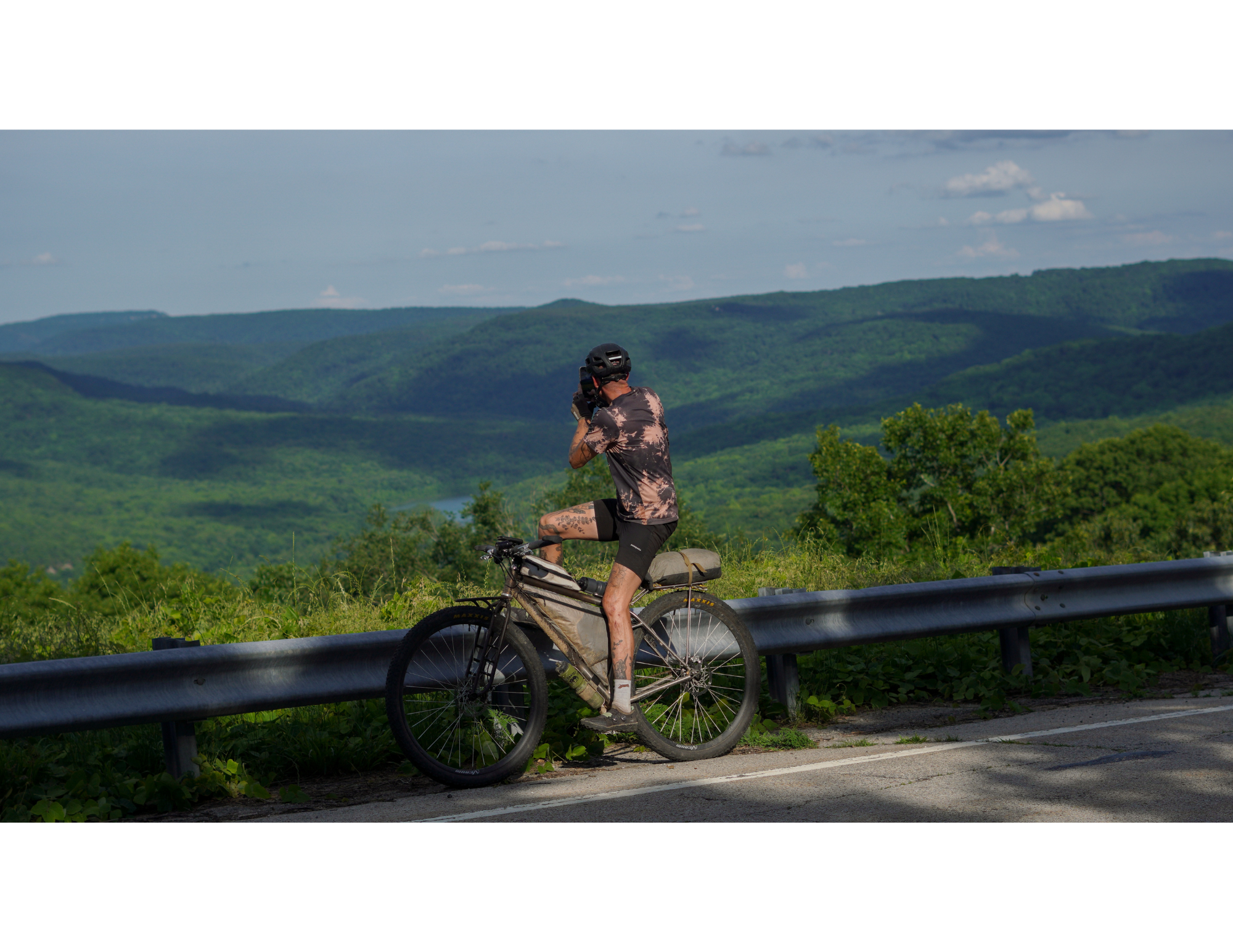 Candid photograph of an ultra bikepacker stopping to take a photograph of rolling hills and mountains in arkansas during the fayetteville ultra circuit