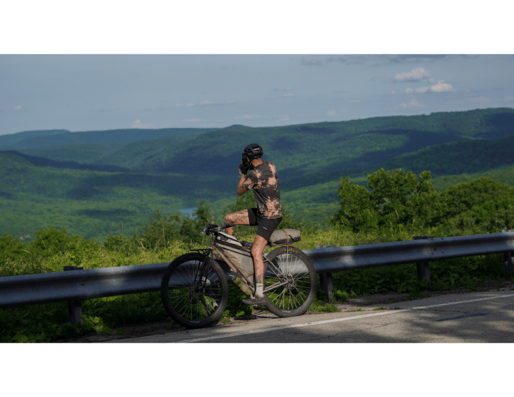 Candid photograph of an ultra bikepacker stopping to take a photograph of rolling hills and mountains in arkansas during the fayetteville ultra circuit