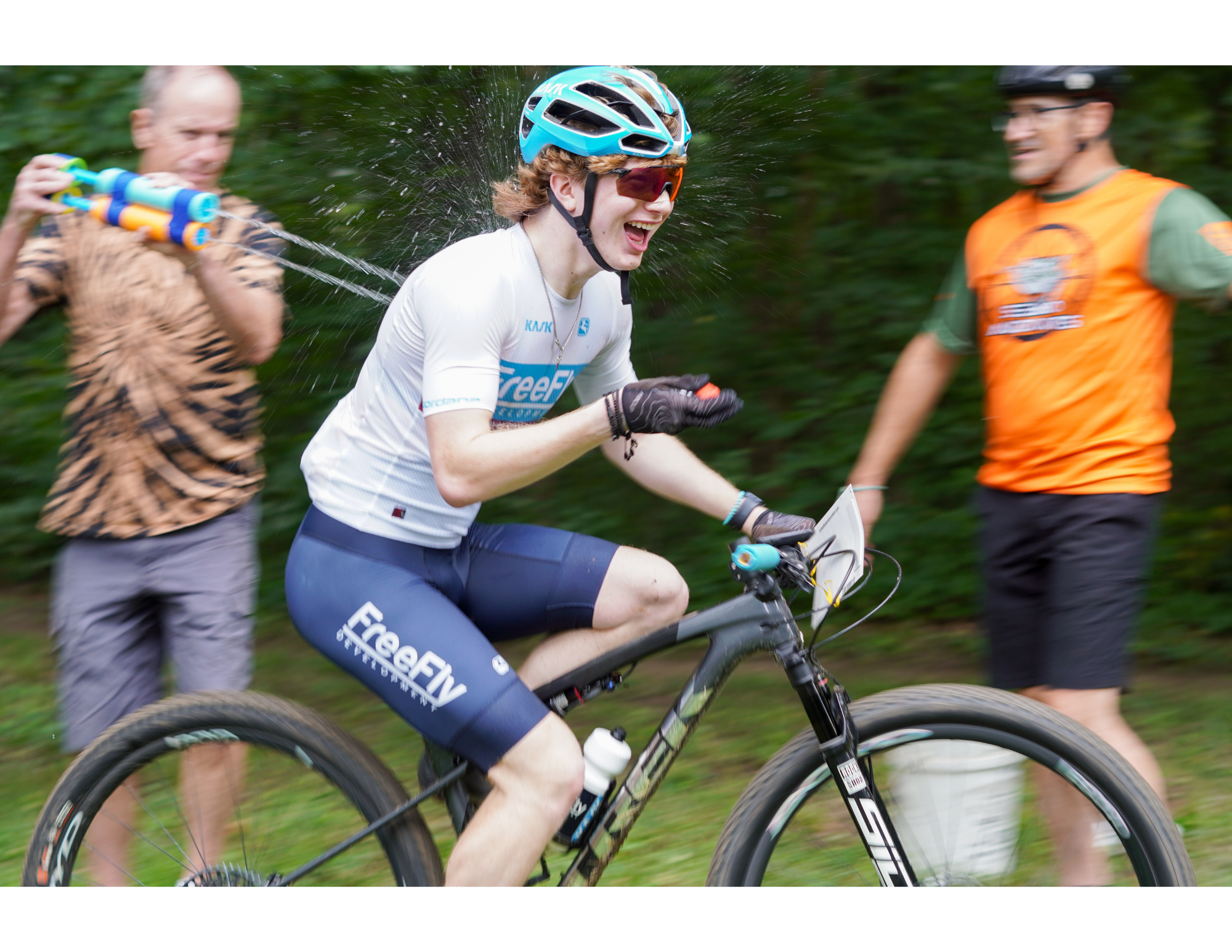 candid action shot of mountain biker getting squirted with a water gun while riding by and holding a piece of watermelon